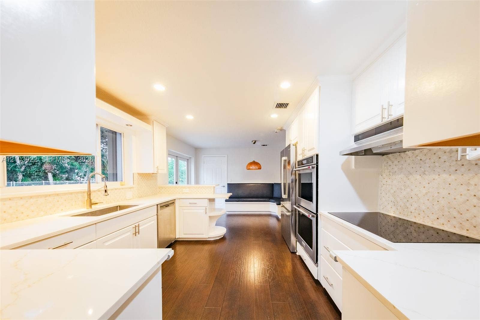White cabinetry with gold-tone hardware, wood-finish flooring, recessed lighting, double wall ovens, and a built-in banquette seating area