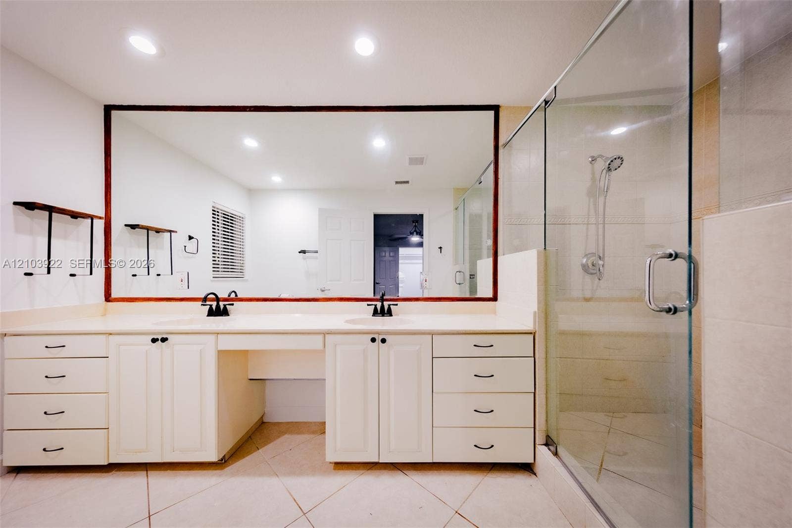 Dual vanity with undermount sinks, expansive mirror, glass-enclosed shower, and built-in cabinetry