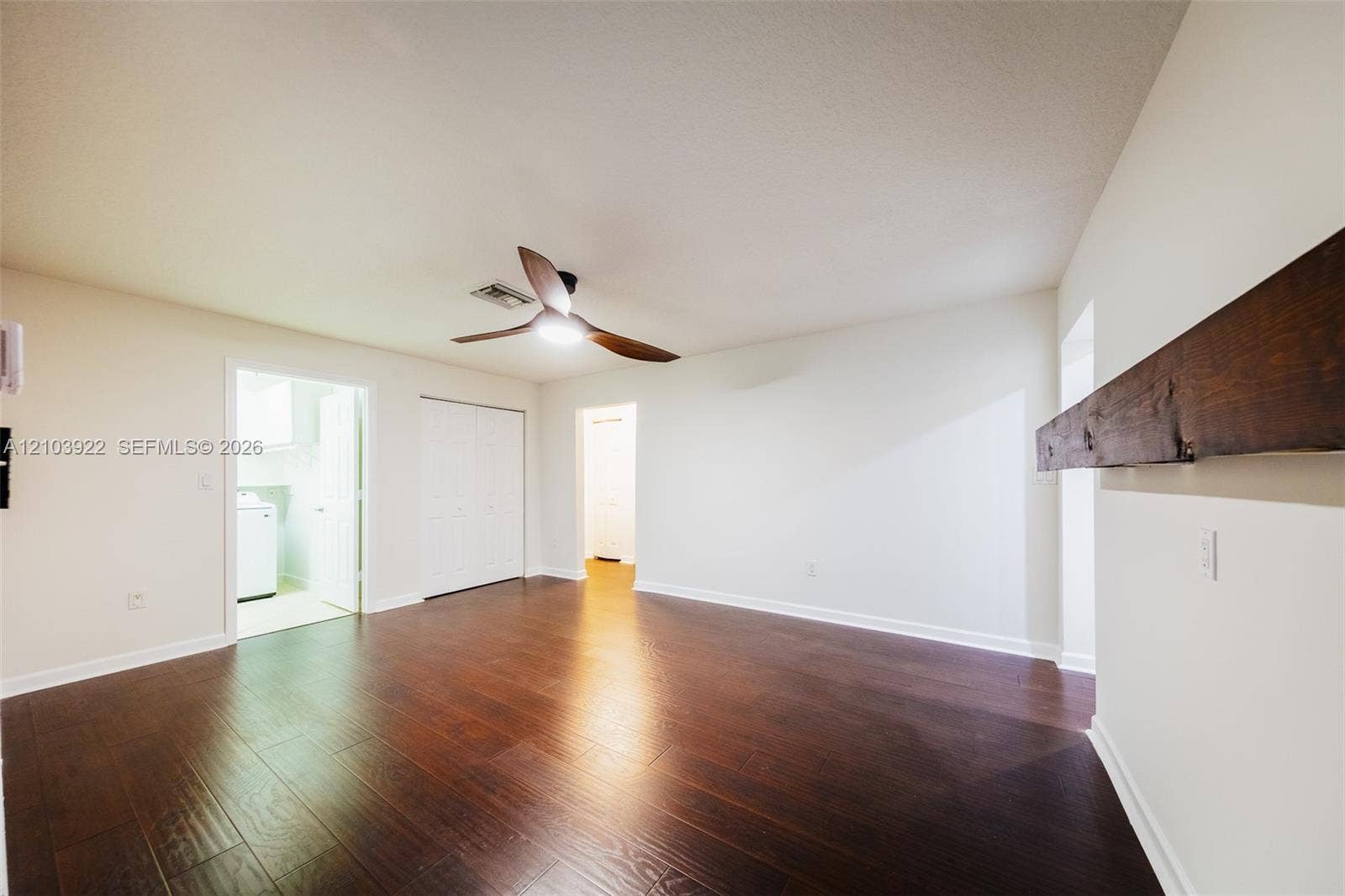 Hardwood-finish flooring, white painted walls, ceiling fan, bi-fold closet doors, and a wood beam mantel
