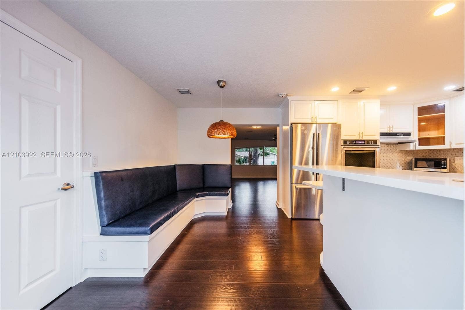 Built-in banquette seating with dark upholstery, wood-finish flooring, white kitchen cabinetry with stainless steel appliances, and a kitchen island with an extended counter