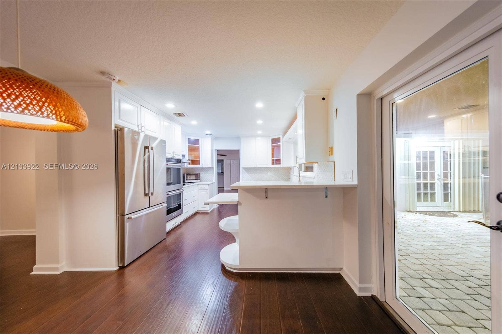 Wood-finish flooring throughout, white cabinetry, stainless steel appliances, recessed lighting, and patio access with glass paneled doors