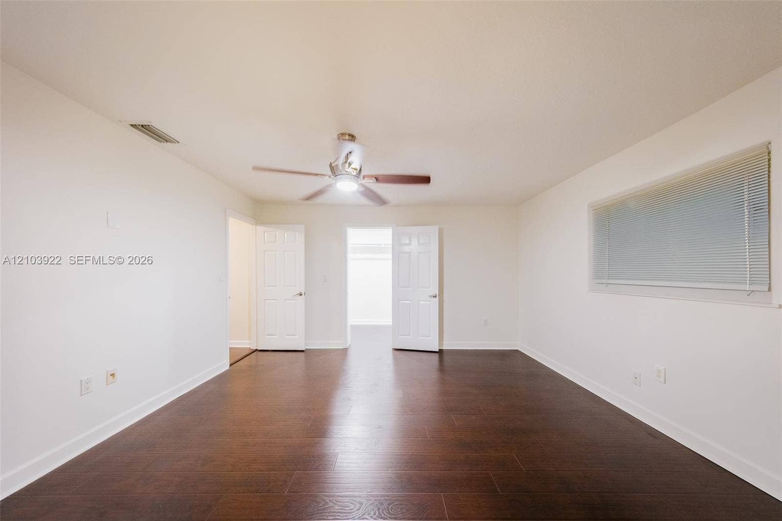 Spacious interior featuring wood-finish flooring, a ceiling fan with integrated lighting, and a large window with blinds