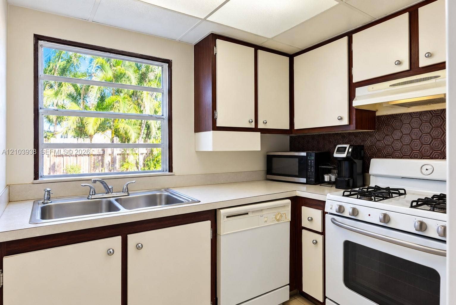 11335 SW 71st Lane, Miami, FL 33173 Kitchen featuring two-tone cabinetry, honeycomb patterned backsplash, double-basin stainless steel sink, and gas range