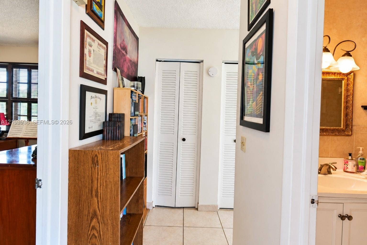 11335 SW 71st Lane, Miami, FL 33173 Hallway featuring light-toned tile flooring, dual white louvered-panel closet doors, and a vanity area equipped with a wall-mounted light fixture and stone-surface countertop