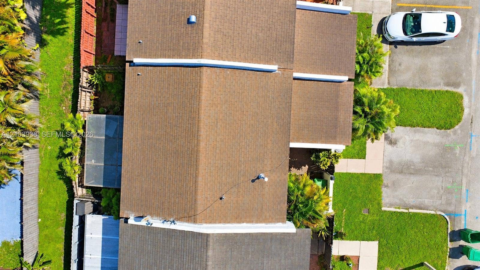 11335 SW 71st Lane, Miami, FL 33173 Aerial perspective of multi-pitch shingle roof featuring an enclosed patio structure, mature perimeter landscaping, concrete hardscaping, and dedicated parking