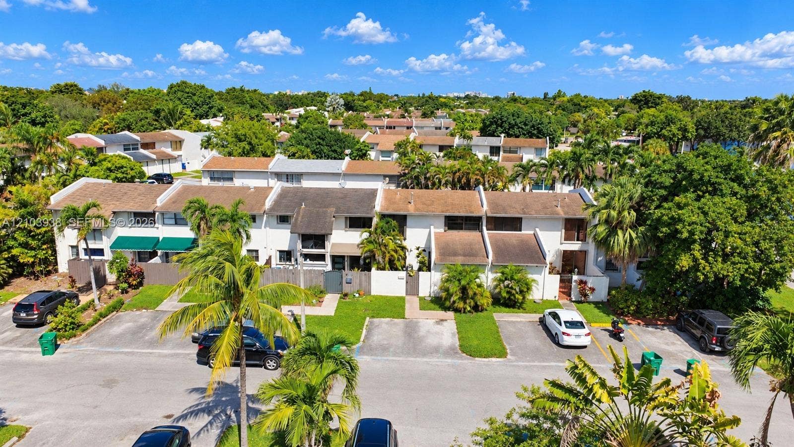 11335 SW 71st Lane, Miami, FL 33173 Multi-level townhome exterior featuring a neutral stucco facade, individual private entrance courtyards, pitched shingle roofing, and dedicated surface parking