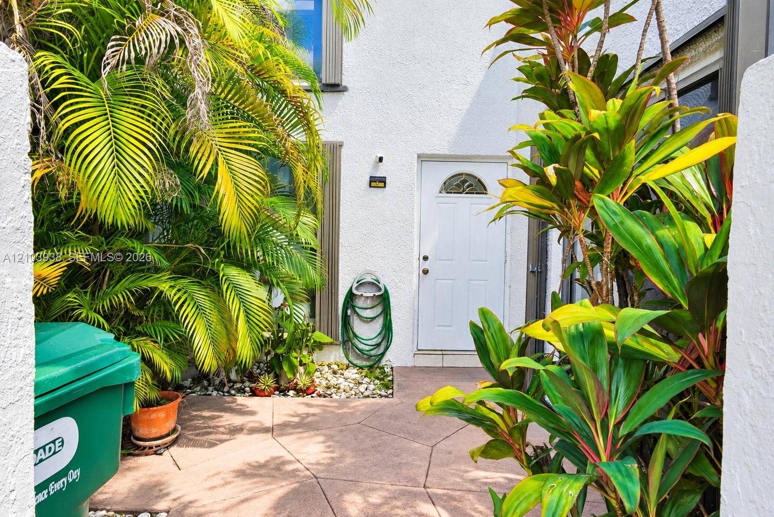 11335 SW 71st Lane, Miami, FL 33173 Stucco exterior featuring an arched-top entry door, stone-finish paving, and mature tropical landscaping