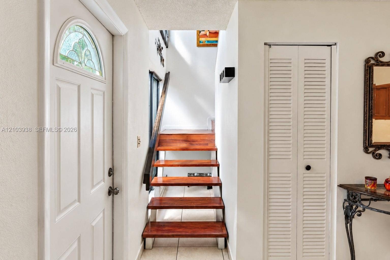 11335 SW 71st Lane, Miami, FL 33173 Entryway featuring an arched front door with decorative glass inlay, open-riser staircase with wood-finish treads, and floor-to-ceiling louvered closet doors