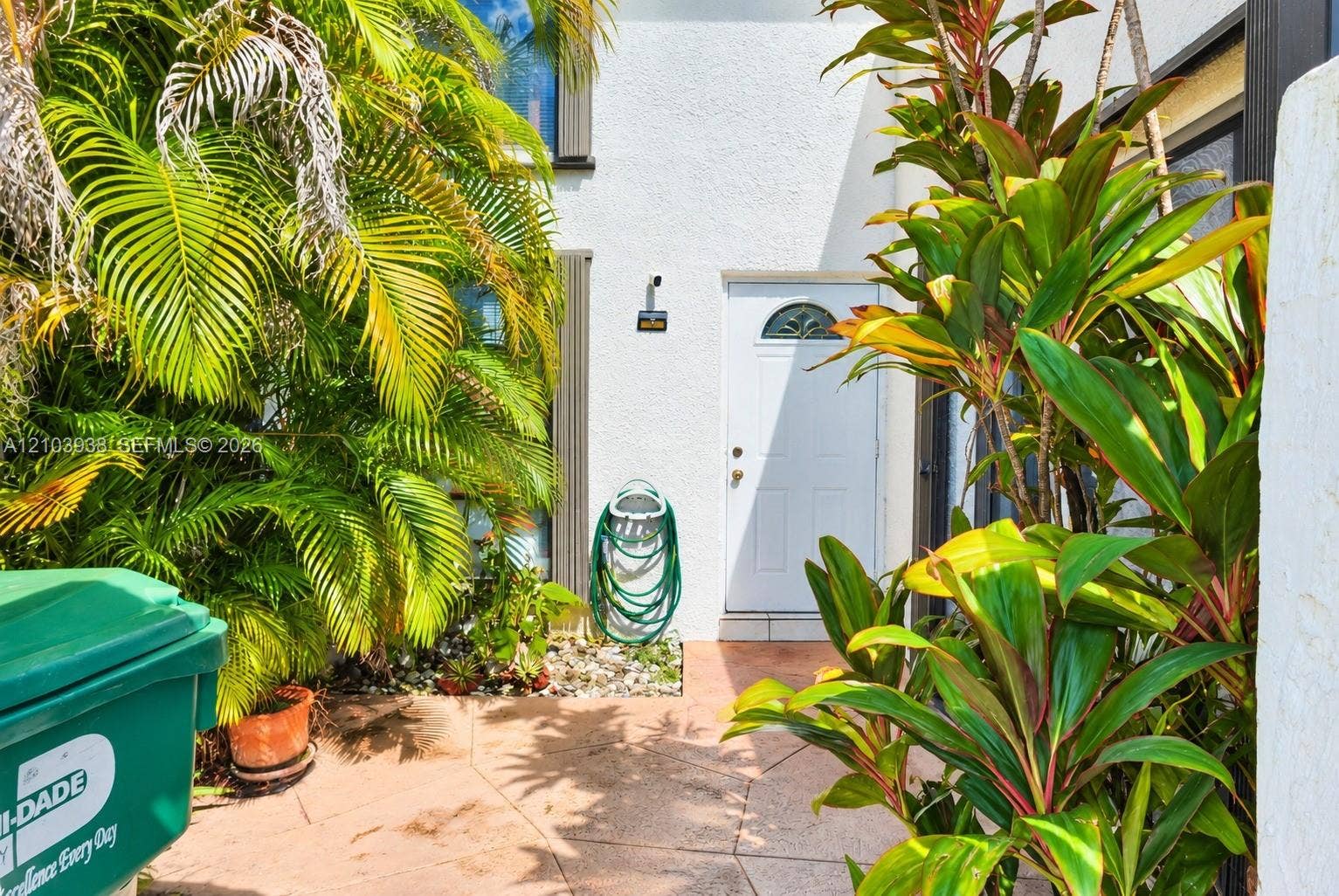 11335 SW 71st Lane, Miami, FL 33173 Exterior entryway featuring a white-finish door with an arched glass inset, paved stone patio, and mature palm landscaping