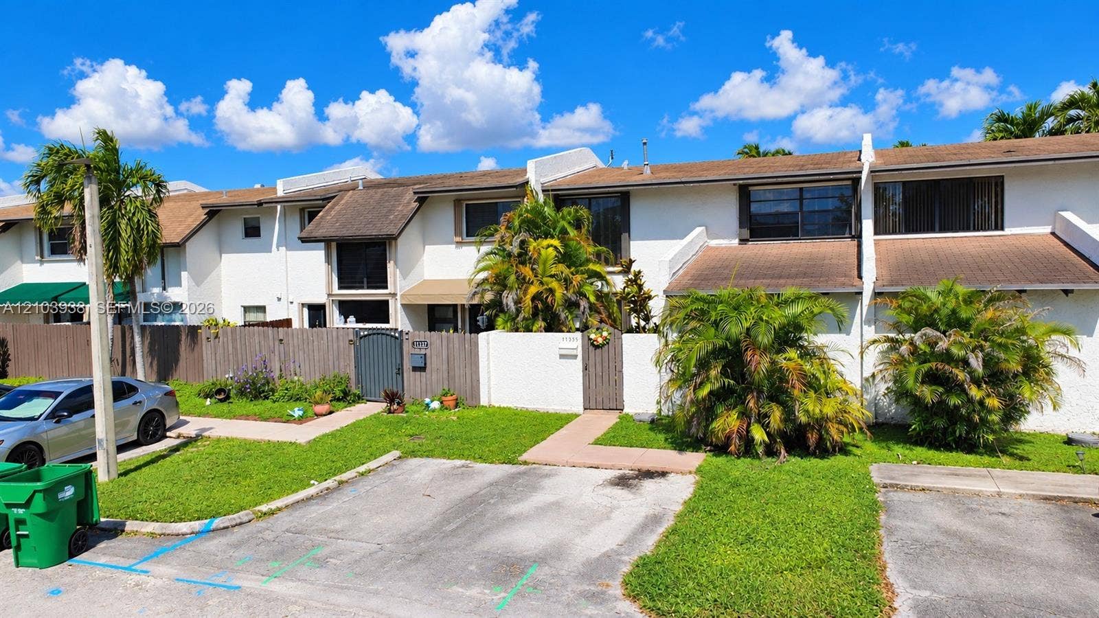 11335 SW 71st Lane, Miami, FL 33173 Multi-unit exterior featuring white stucco siding, brown shingle roofing, private fenced courtyards, and dedicated paved parking