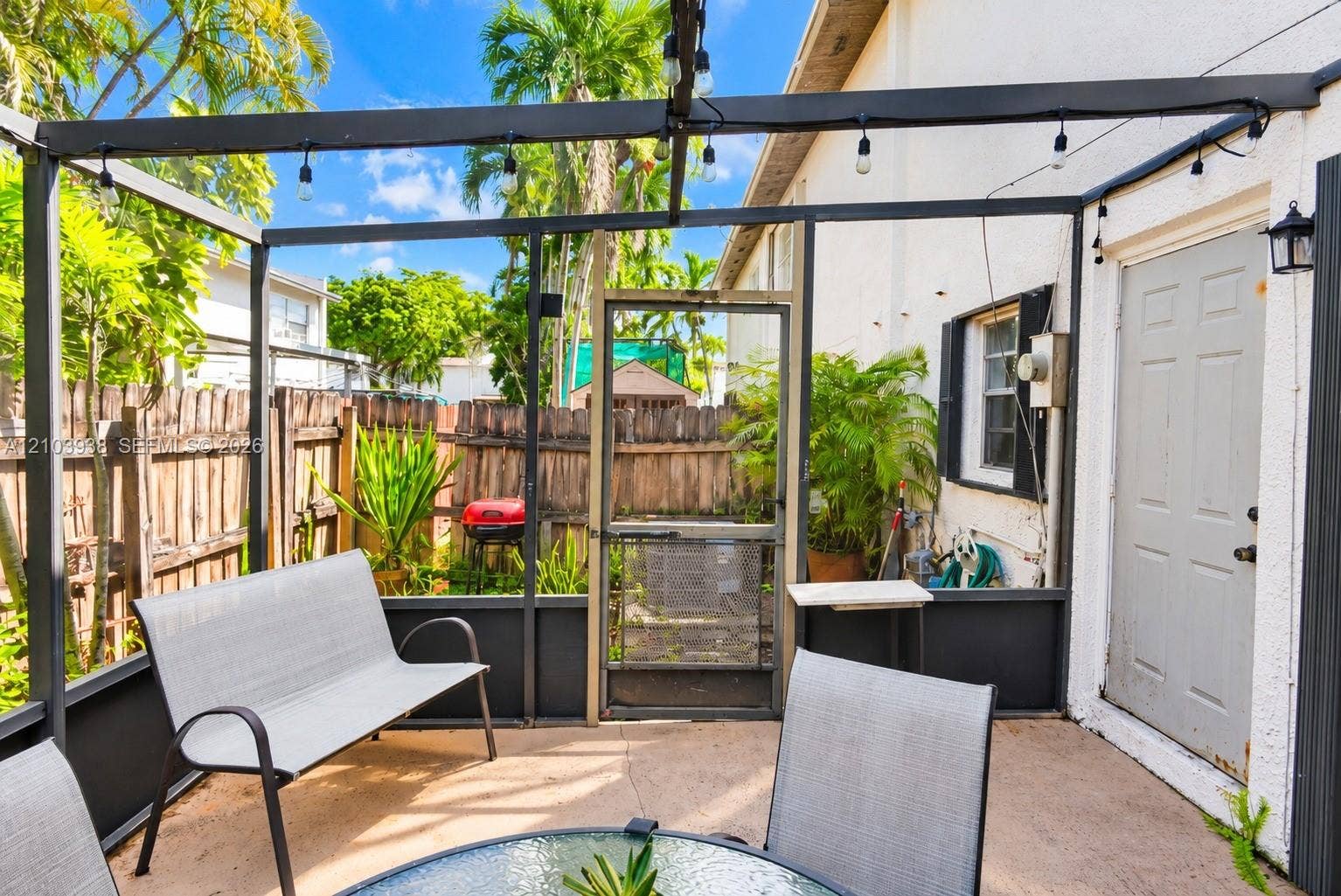 11335 SW 71st Lane, Miami, FL 33173 Screened-in patio featuring a concrete floor, dark metal structural framing, exterior wall-mounted lighting, and a wood privacy fence