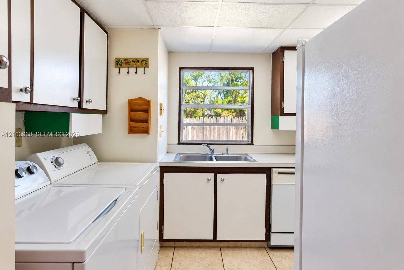 11335 SW 71st Lane, Miami, FL 33173 Laundry area featuring white cabinetry with dark trim, a stainless steel dual-basin sink, tile flooring, and a window providing natural light