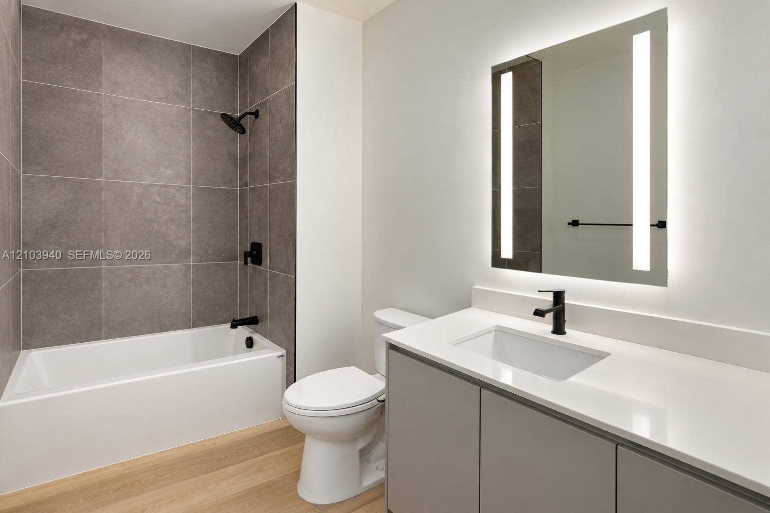 307 SW 5th Street, #2610, Fort Lauderdale, Fort Lauderdale, FL 33315 Bathroom featuring a vanity with a white countertop and integrated sink, a rectangular LED-backlit mirror, wood-finish flooring, and a tub-shower combination with floor-to-ceiling grey tile surround and matte black fixtures