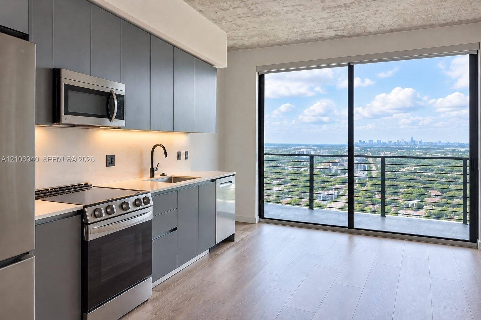 307 SW 5th Street, #2610, Fort Lauderdale, Fort Lauderdale, FL 33315 Modern kitchen featuring matte grey flat-panel cabinetry, light-toned countertops, stainless steel appliances, wood-finish flooring, and floor-to-ceiling glass doors opening to a private balcony