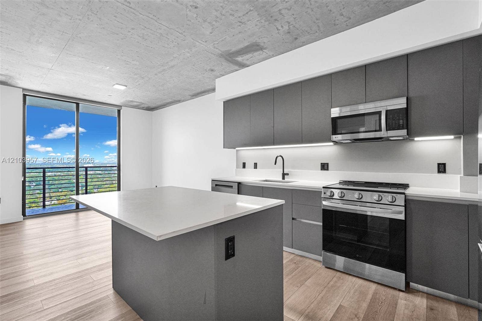 307 SW 5th Street, #0, Fort Lauderdale, Fort Lauderdale, FL 33315 Modern kitchen featuring an island with a light-toned countertop, stainless steel appliances, dark gray cabinetry, and wood-finish flooring
