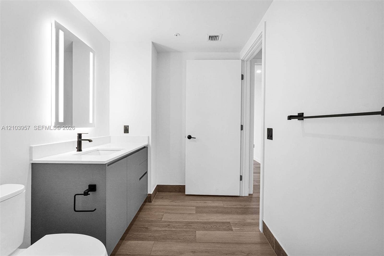 307 SW 5th Street, #0, Fort Lauderdale, Fort Lauderdale, FL 33315 Contemporary bathroom featuring a floating vanity with a white countertop and integrated sink, an illuminated mirror, matte black fixtures, and wood-finish flooring