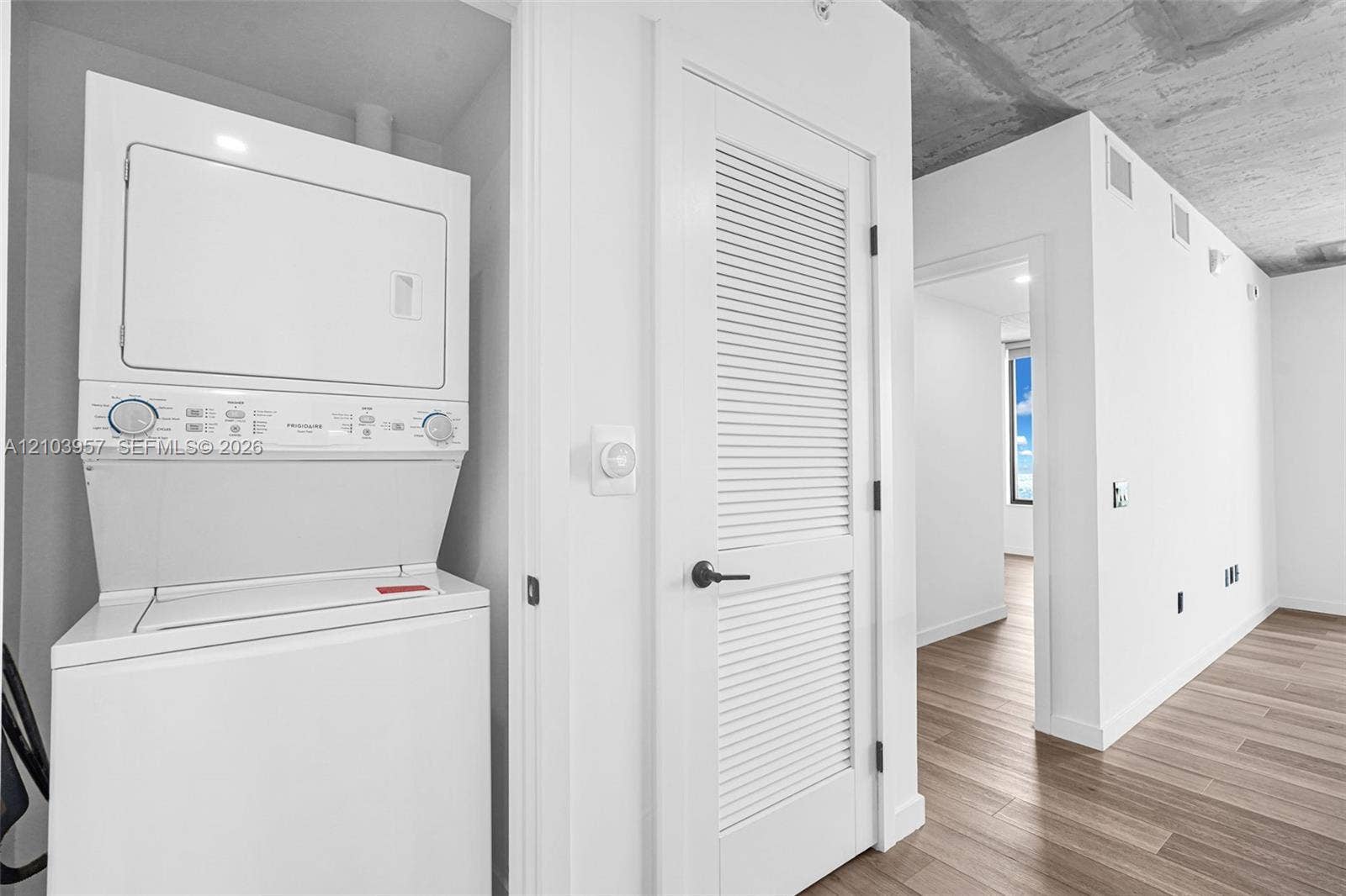 307 SW 5th Street, #0, Fort Lauderdale, Fort Lauderdale, FL 33315 Stacked laundry appliances, louvered interior door, wood-finish flooring, exposed concrete ceiling, and white wall finishes