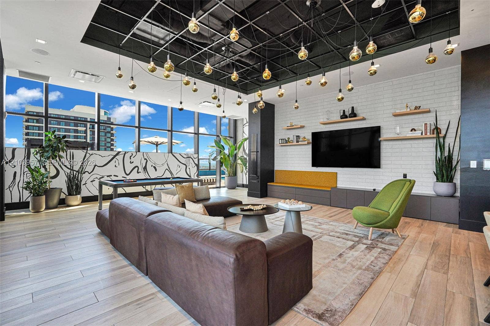 307 SW 5th Street, #0, Fort Lauderdale, Fort Lauderdale, FL 33315 Expansive living area with large windows, wood-finish flooring, white brick-patterned accent wall, built-in shelving, and a unique grid-patterned ceiling with multiple pendant lights