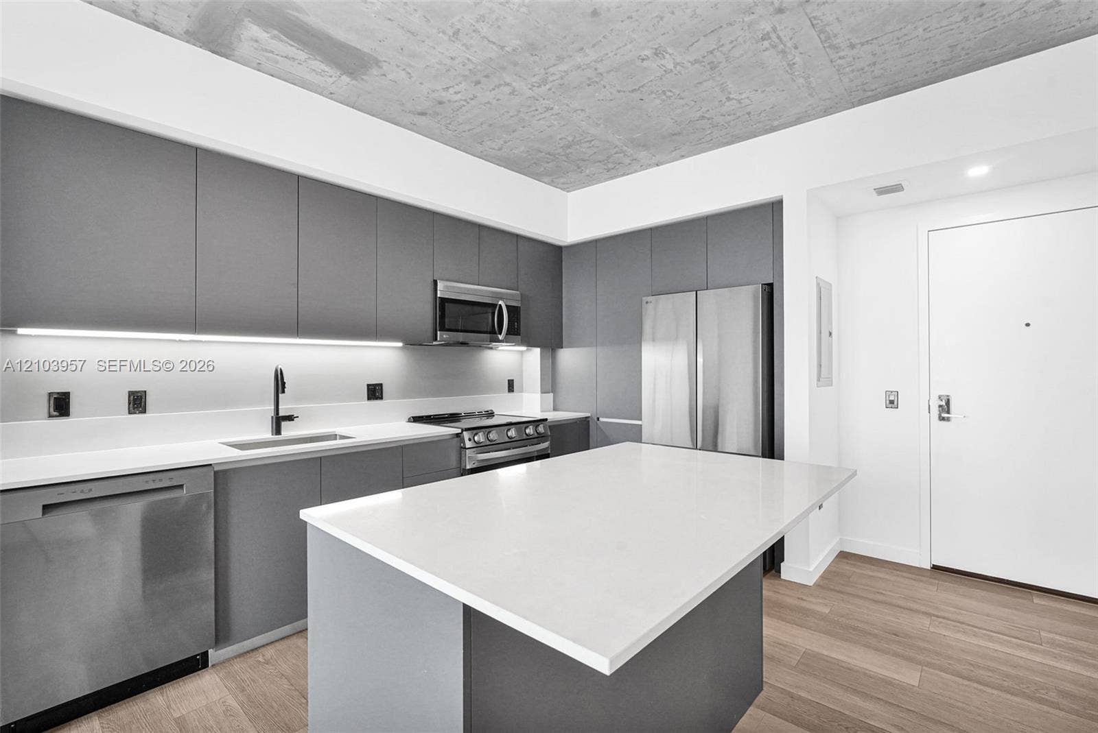 307 SW 5th Street, #0, Fort Lauderdale, Fort Lauderdale, FL 33315 Modern kitchen featuring flat-panel cabinetry, stainless steel appliances, a center island with a light-toned countertop, a stainless steel sink with a dark-toned faucet, and wood-finish flooring