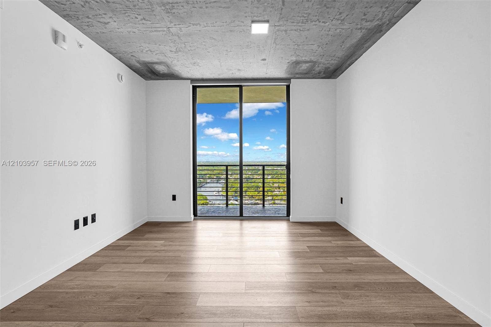 307 SW 5th Street, #0, Fort Lauderdale, Fort Lauderdale, FL 33315 Expansive room with wood-finish flooring, a full-height glass sliding door, and a private balcony with metal railings