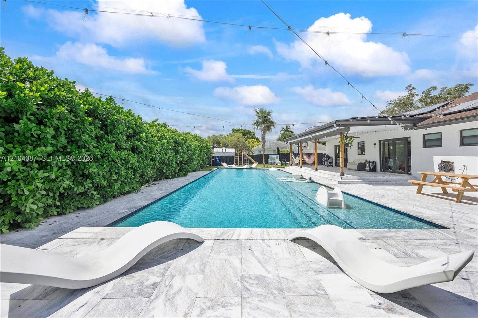 8840 SW 181st Terrace, Palmetto Bay, FL 33157 Expansive outdoor living area featuring a rectangular swimming pool, large patio with light-toned pavers, and a covered patio structure