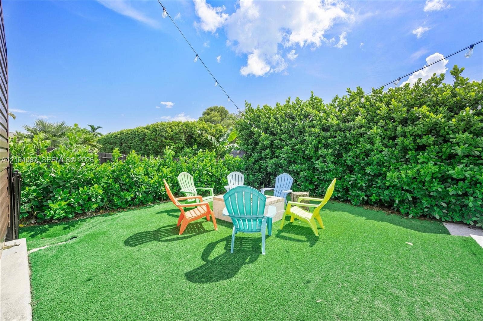 Artificial turf backyard with a fire pit, privacy hedges, and string lighting