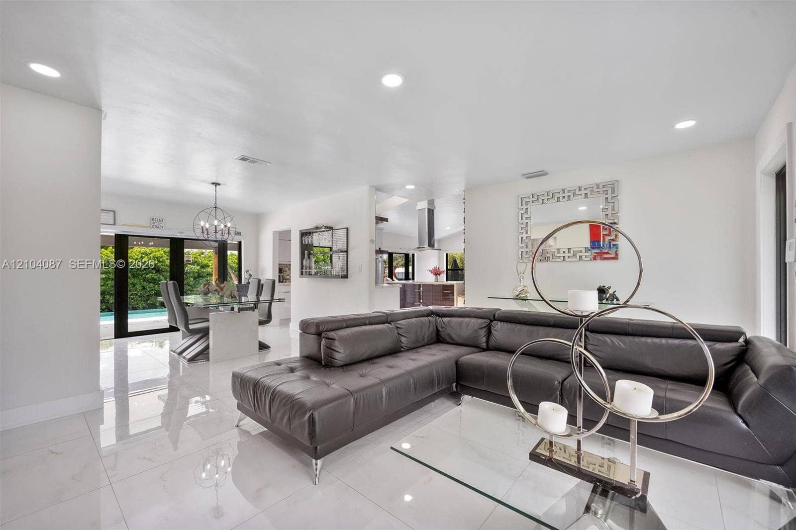 Recessed ceiling lighting, glossy white flooring, modern glass dining table, contemporary chandelier, and sliding glass doors