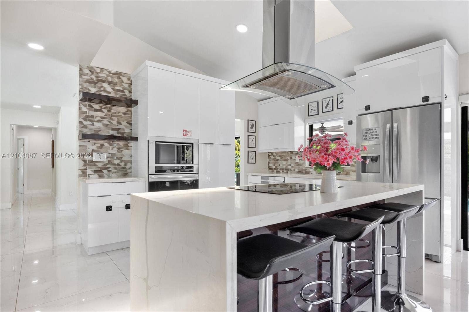 Gourmet kitchen featuring a waterfall island, stainless steel appliances, white high-gloss cabinetry, and a decorative tile accent wall