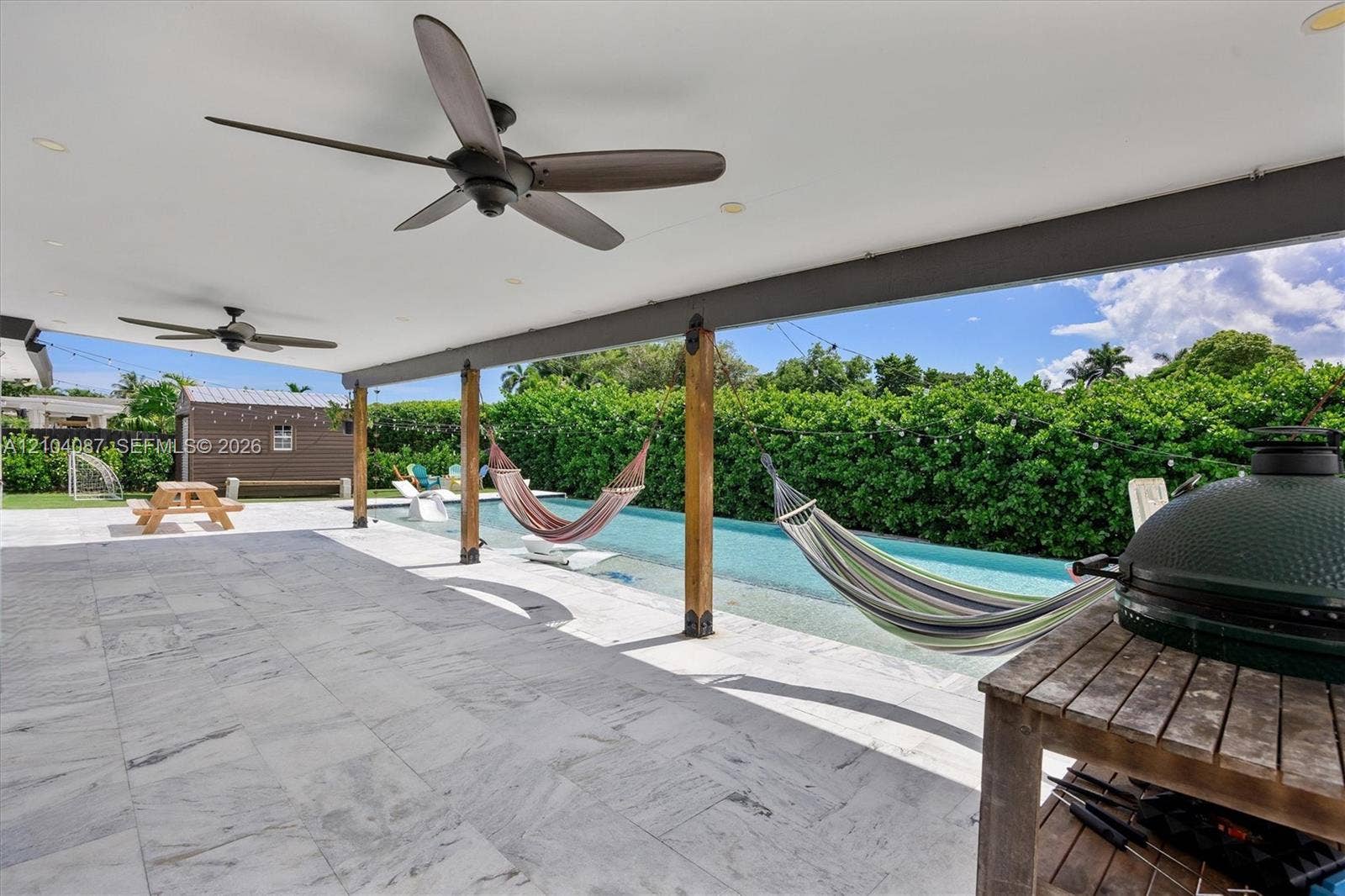 Covered patio with integrated ceiling fans, a full-length swimming pool, and a stone tile outdoor surface