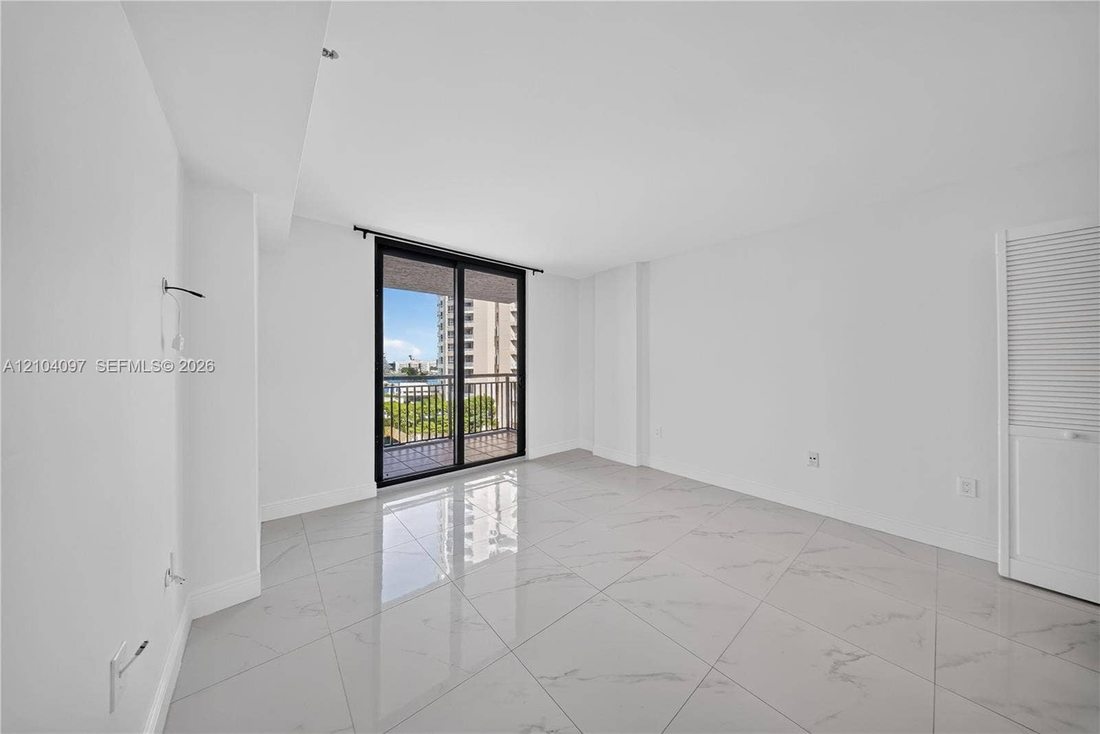 540 Brickell Key Drive, #916, Miami, Miami, FL 33131 Interior space featuring oversized light-toned tile flooring, large sliding glass doors, a private balcony with metal railing, and louvered-style closet doors