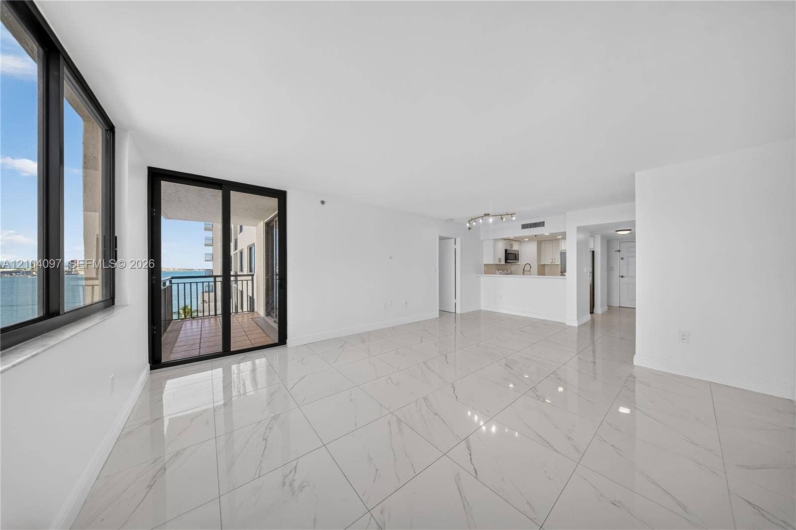 540 Brickell Key Drive, #916, Miami, Miami, FL 33131 Open-concept living space featuring large-format polished tile flooring, floor-to-ceiling windows, sliding glass door access to a balcony, and white cabinetry in the kitchen area