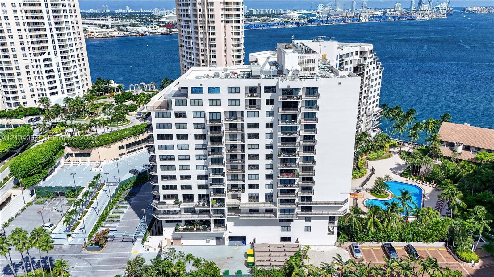 540 Brickell Key Drive, #916, Miami, Miami, FL 33131 High-rise residential building featuring stacked private balconies, an on-site swimming pool, paved surface parking, and extensive tropical landscaping situated on the waterfront