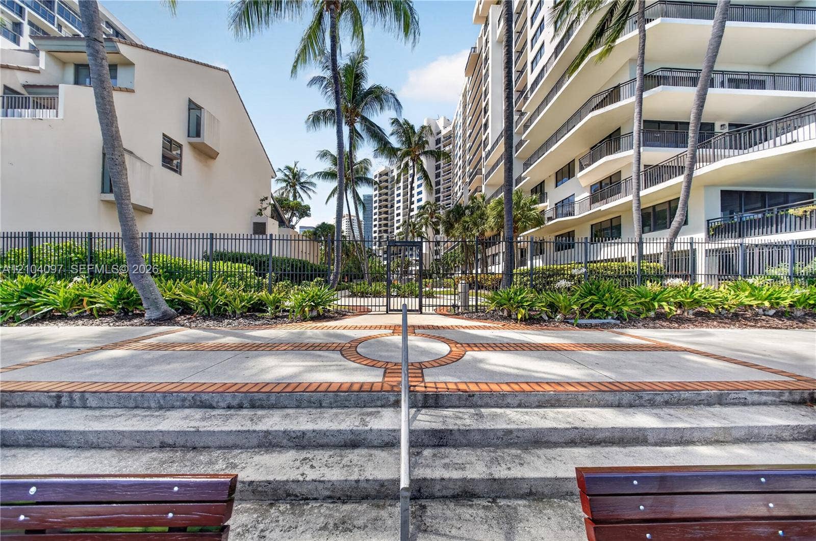 540 Brickell Key Drive, #916, Miami, Miami, FL 33131 Concrete patio with inlaid brick detailing, metal perimeter fencing, tiered concrete steps with a central handrail, and mature palm trees