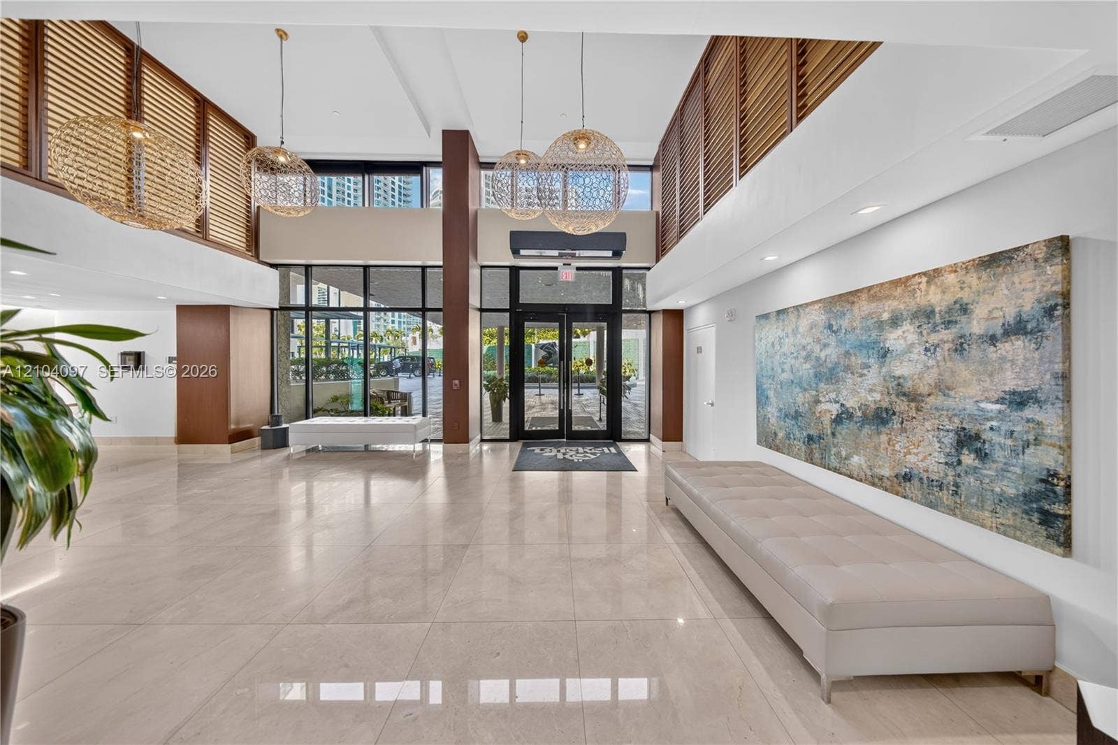 540 Brickell Key Drive, #916, Miami, Miami, FL 33131 Grand lobby entrance featuring polished stone flooring, double-height ceilings, floor-to-ceiling glass paneling, decorative woven pendant lighting, and slatted wood-finish accent walls