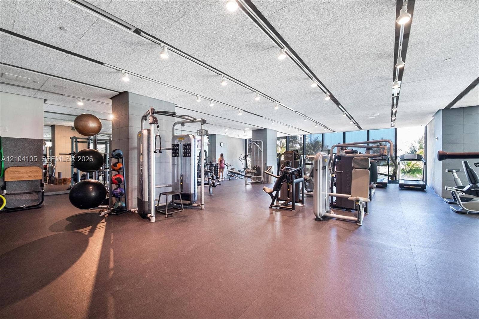 Expansive fitness center with track lighting, multiple exercise machines, and extensive window walls