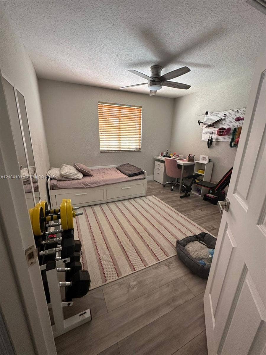 Room featuring wood-finish flooring, a ceiling fan with integrated lighting, and a window with blinds