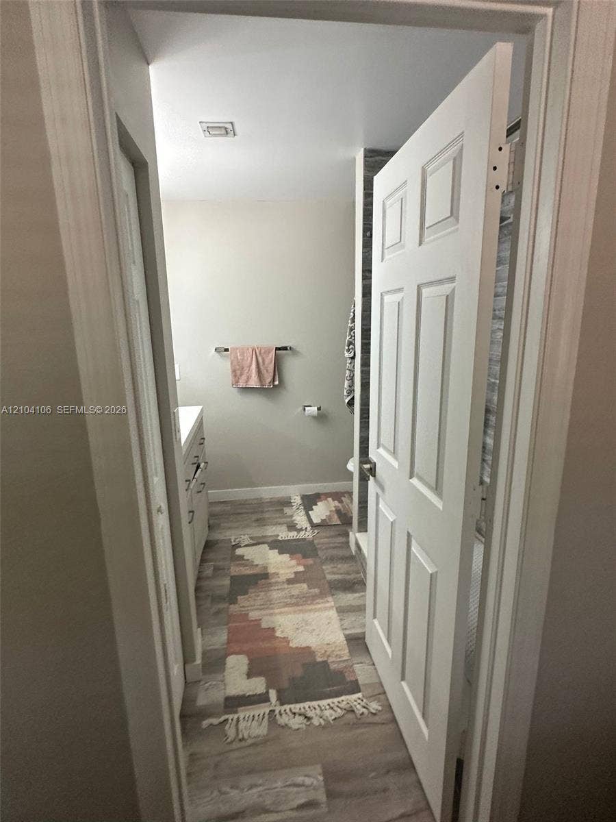 Bathroom featuring wood-finish flooring, a white six-panel door, and vanity cabinetry with metallic hardware