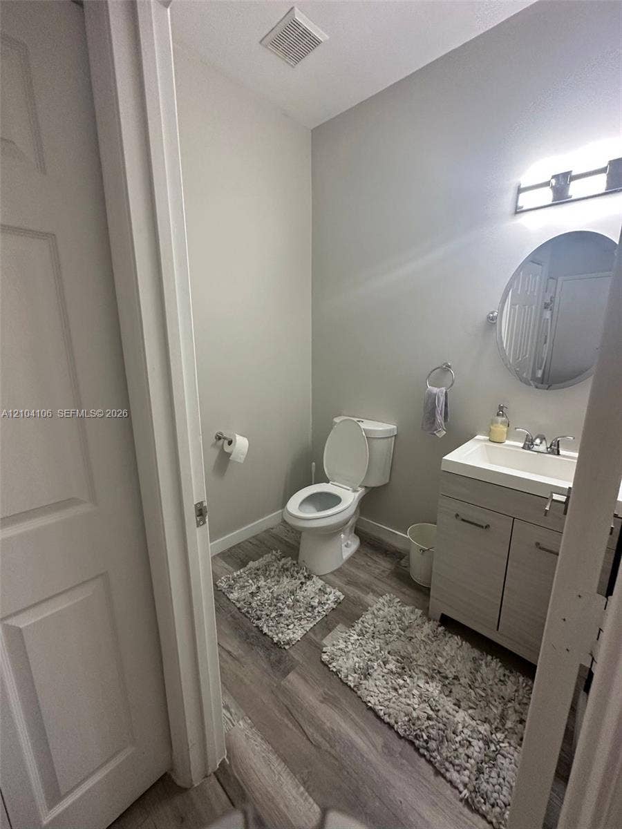Bathroom featuring wood-finish flooring, a vanity with a rectangular sink, wall-mounted lighting, and an oval mirror