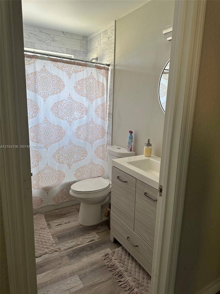 Bathroom featuring a wood-finish vanity with an integrated sink, wood-finish flooring, and a tub enclosure with tile-patterned wall surround