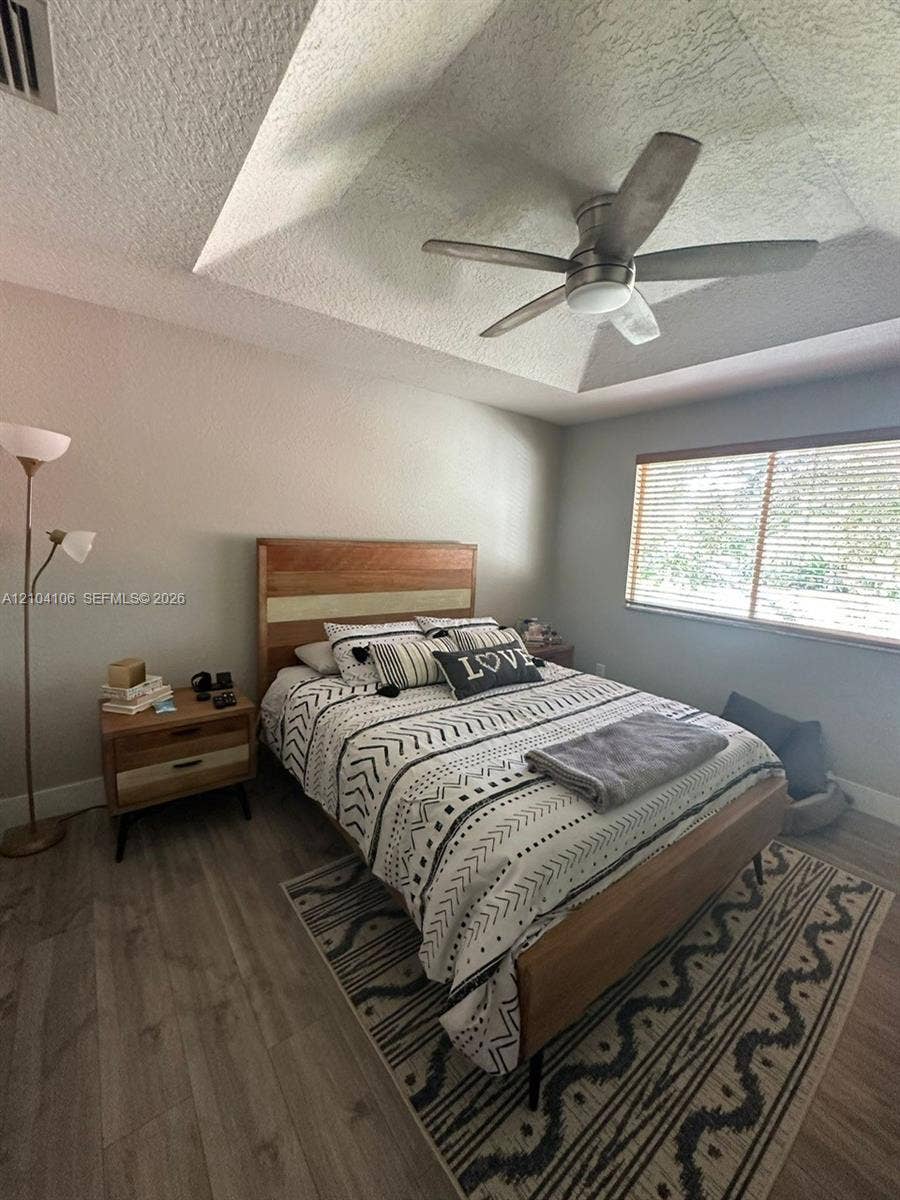 Tray ceiling with a central brushed-nickel ceiling fan, wood-finish flooring, and horizontal window blinds