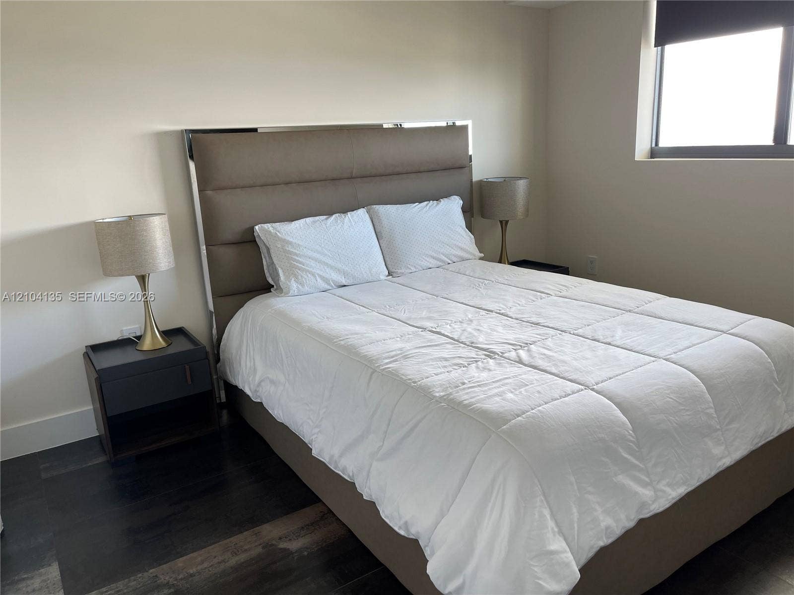 Neutral-toned walls paired with dark wood-finish flooring and a single-pane window featuring a retractable shade