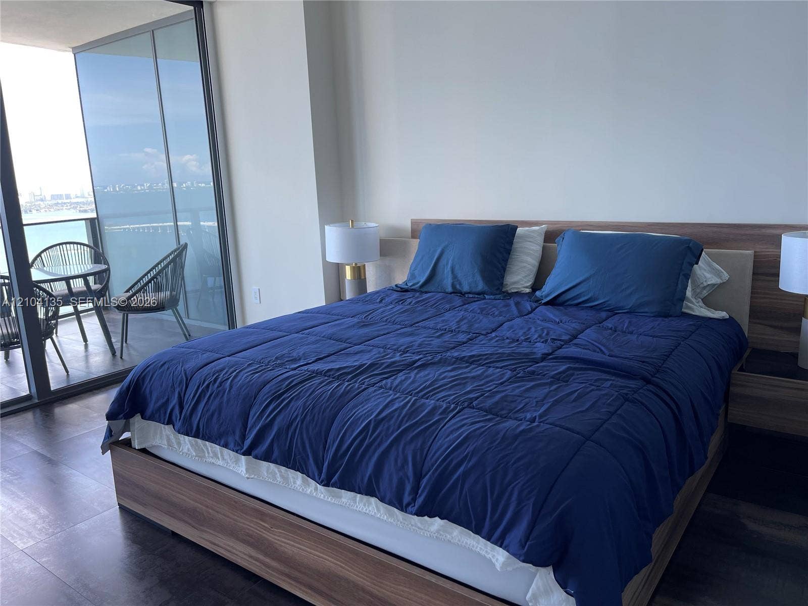 Floor-to-ceiling glass sliding doors, wood-finish platform bed frame with integrated headboard, and dark-toned flooring