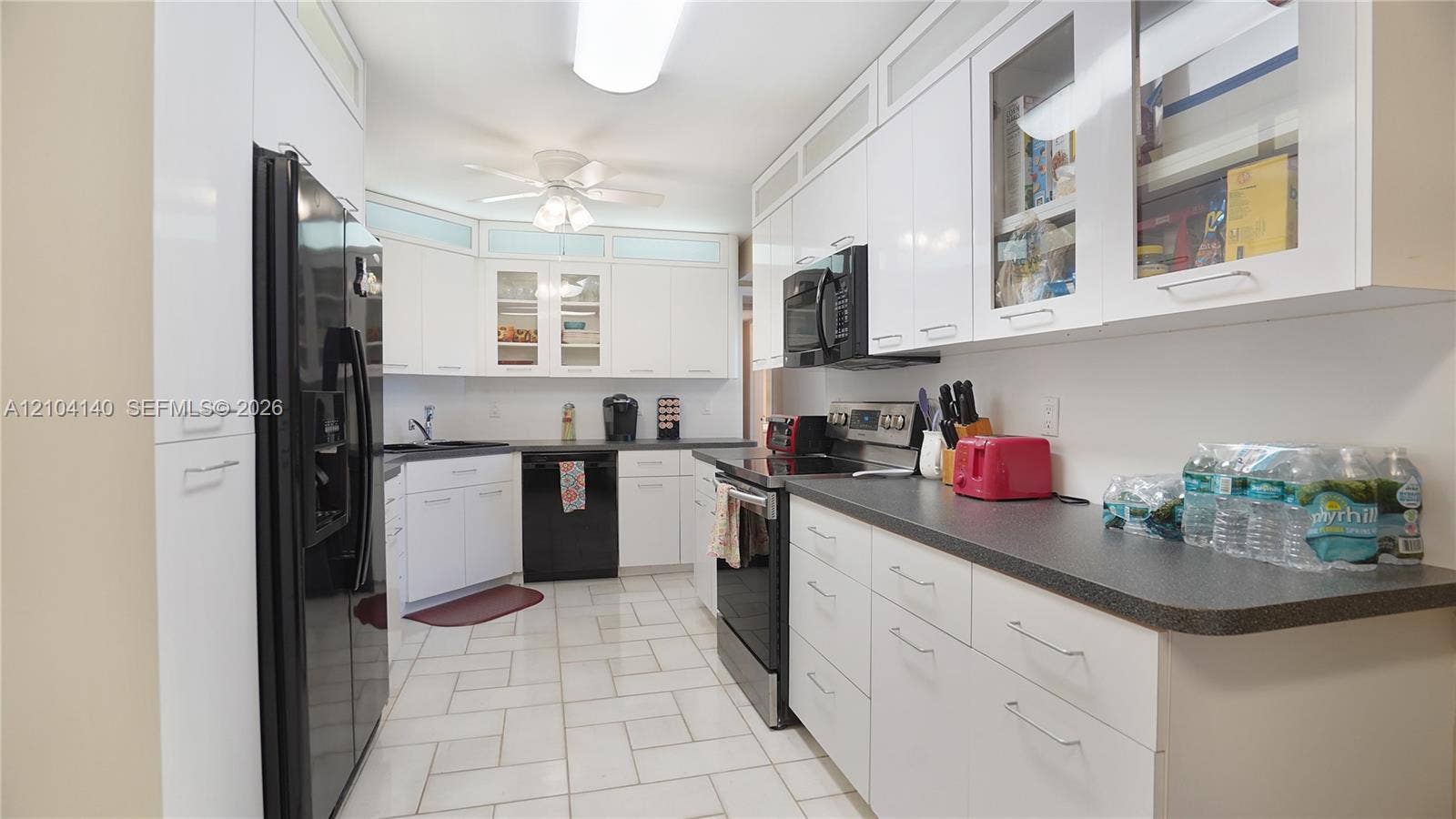 111 N Pompano Beach Boulevard, #304, Pompano Beach, FL 33062 Kitchen featuring white cabinetry with glass-front uppers, solid surface countertops, tiled flooring, and integrated black appliances