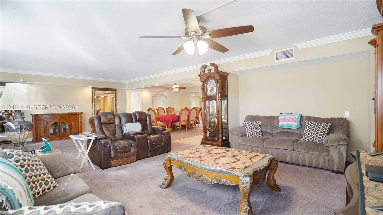 111 N Pompano Beach Boulevard, #304, Pompano Beach, FL 33062 Spacious living area featuring crown molding, neutral wall color, carpeted flooring, and a ceiling-mounted light fixture with a fan