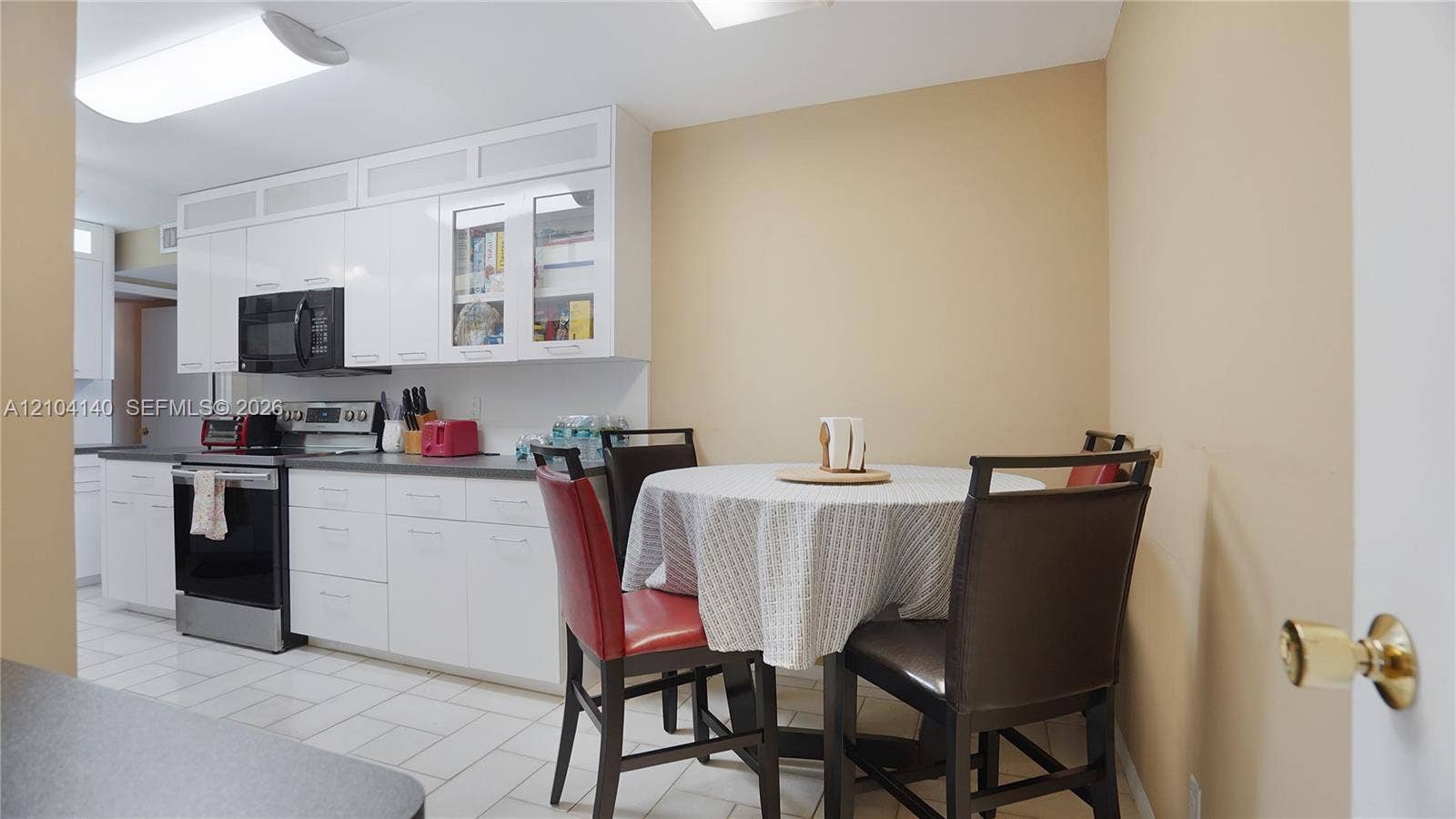 111 N Pompano Beach Boulevard, #304, Pompano Beach, FL 33062 Kitchen featuring high-gloss white cabinetry, glass-paneled upper cabinets, stainless steel appliances, and ceramic tile flooring