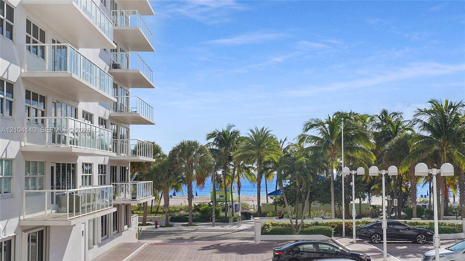 111 N Pompano Beach Boulevard, #304, Pompano Beach, FL 33062 Multi-story building featuring stacked balconies with glass railings, paved ground-level lot, and mature palm trees