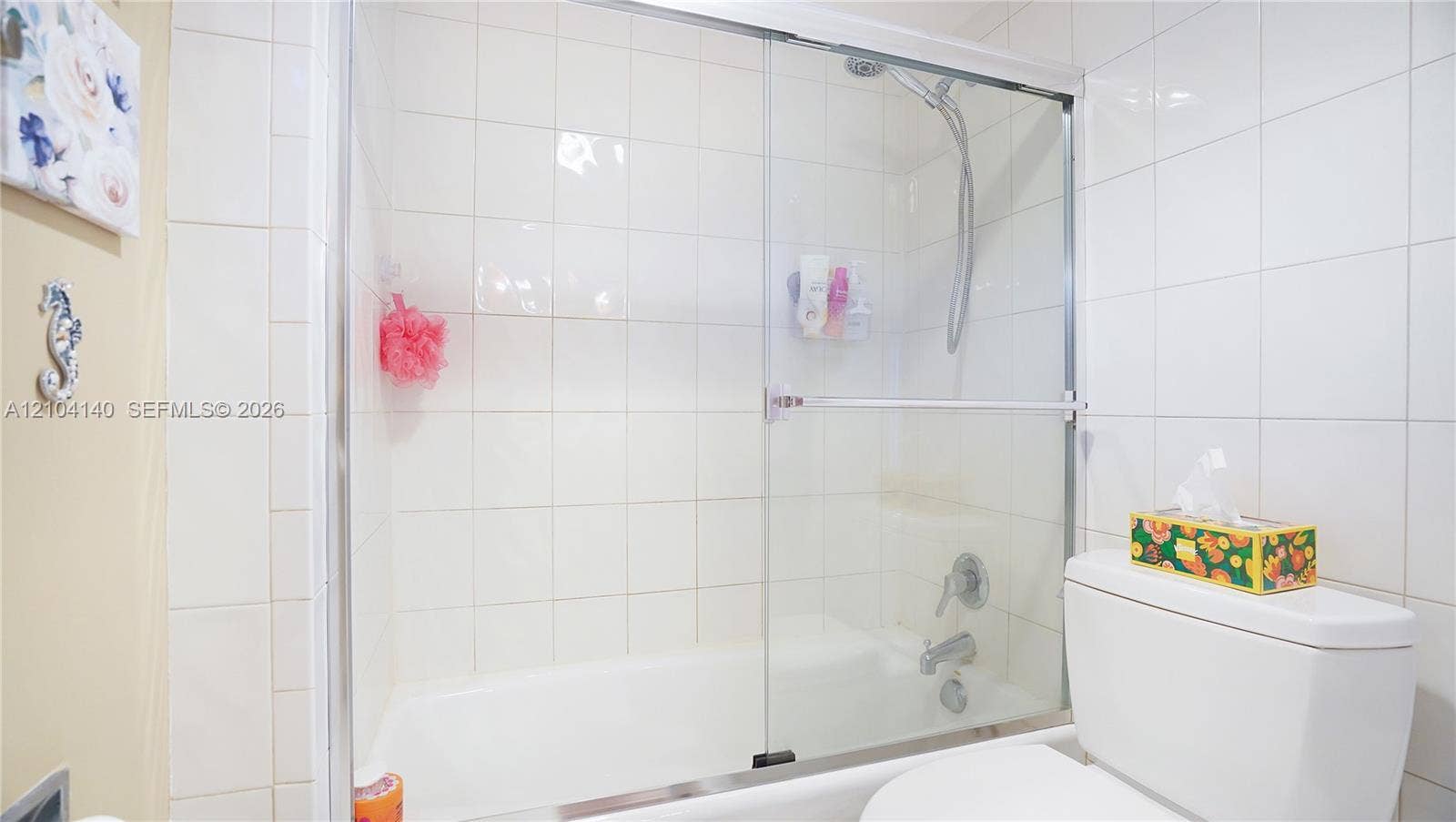 111 N Pompano Beach Boulevard, #304, Pompano Beach, FL 33062 Bathtub and shower combination featuring full-height white wall tiling, sliding glass enclosure, chrome fixtures, and a handheld shower head