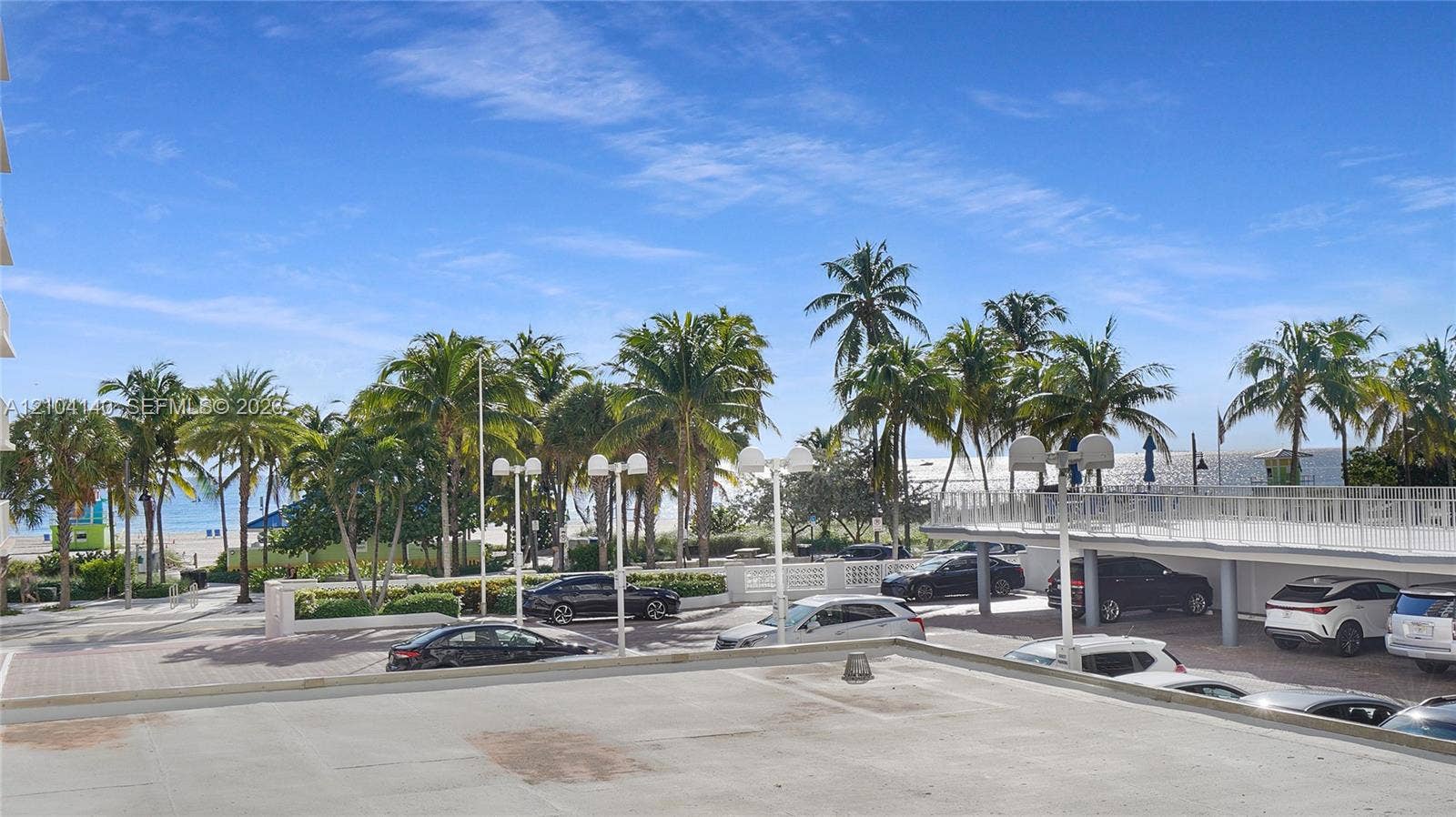 111 N Pompano Beach Boulevard, #304, Pompano Beach, FL 33062 Outdoor terrace featuring a paved surface and white metal railing, overlooking a landscaped lot with mature palm trees and coastal scenery