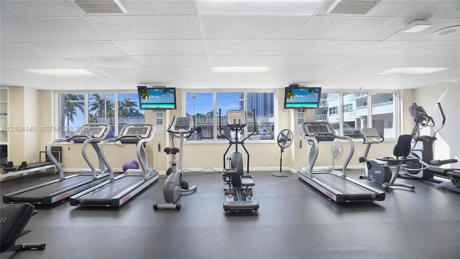 111 N Pompano Beach Boulevard, #304, Pompano Beach, FL 33062 Fitness area featuring large-format windows, grid-pattern drop ceiling, and resilient rubber flooring