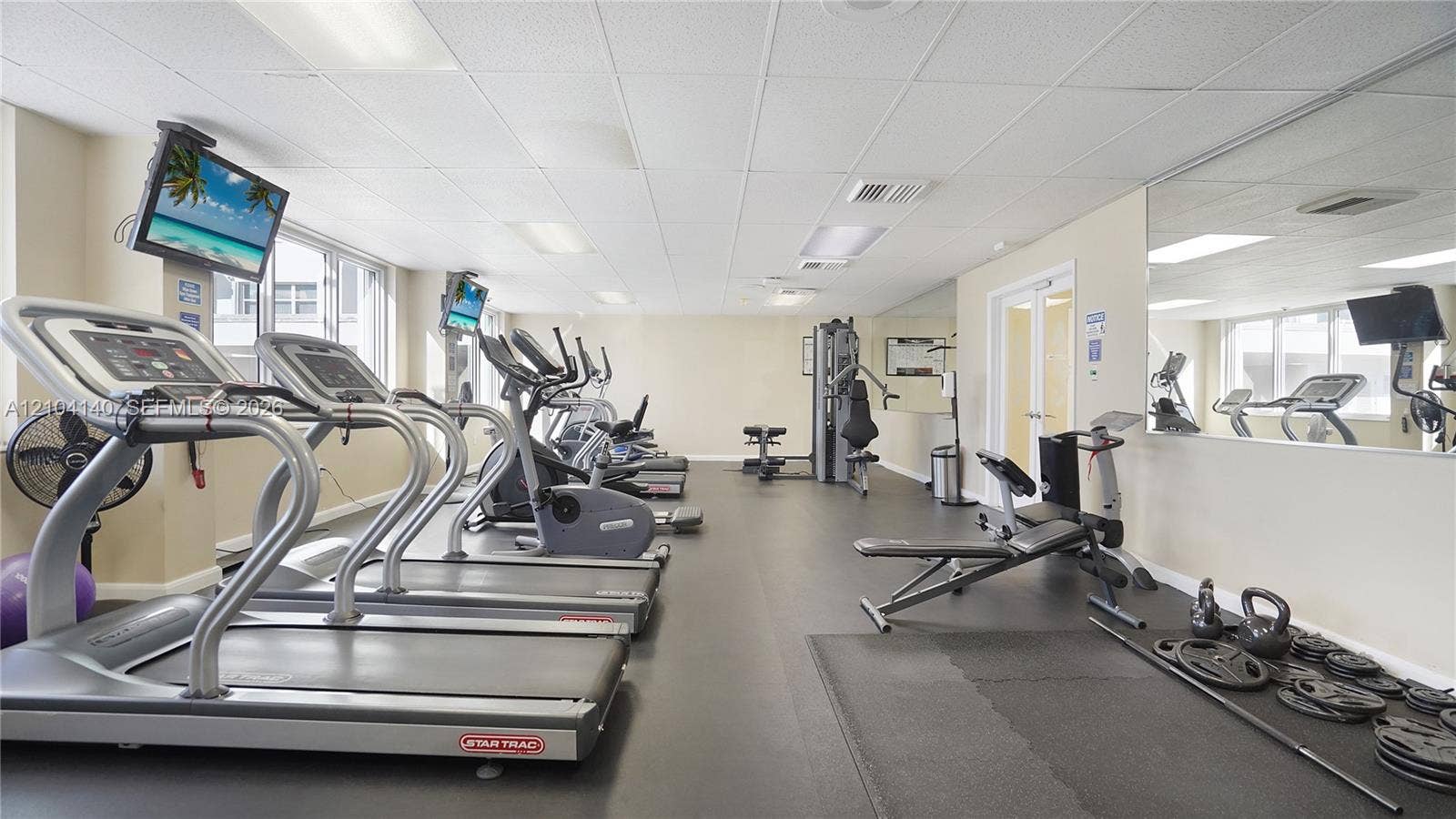 111 N Pompano Beach Boulevard, #304, Pompano Beach, FL 33062 Fitness center featuring rubber flooring, wall-mounted mirrored panels, and drop ceiling with recessed lighting